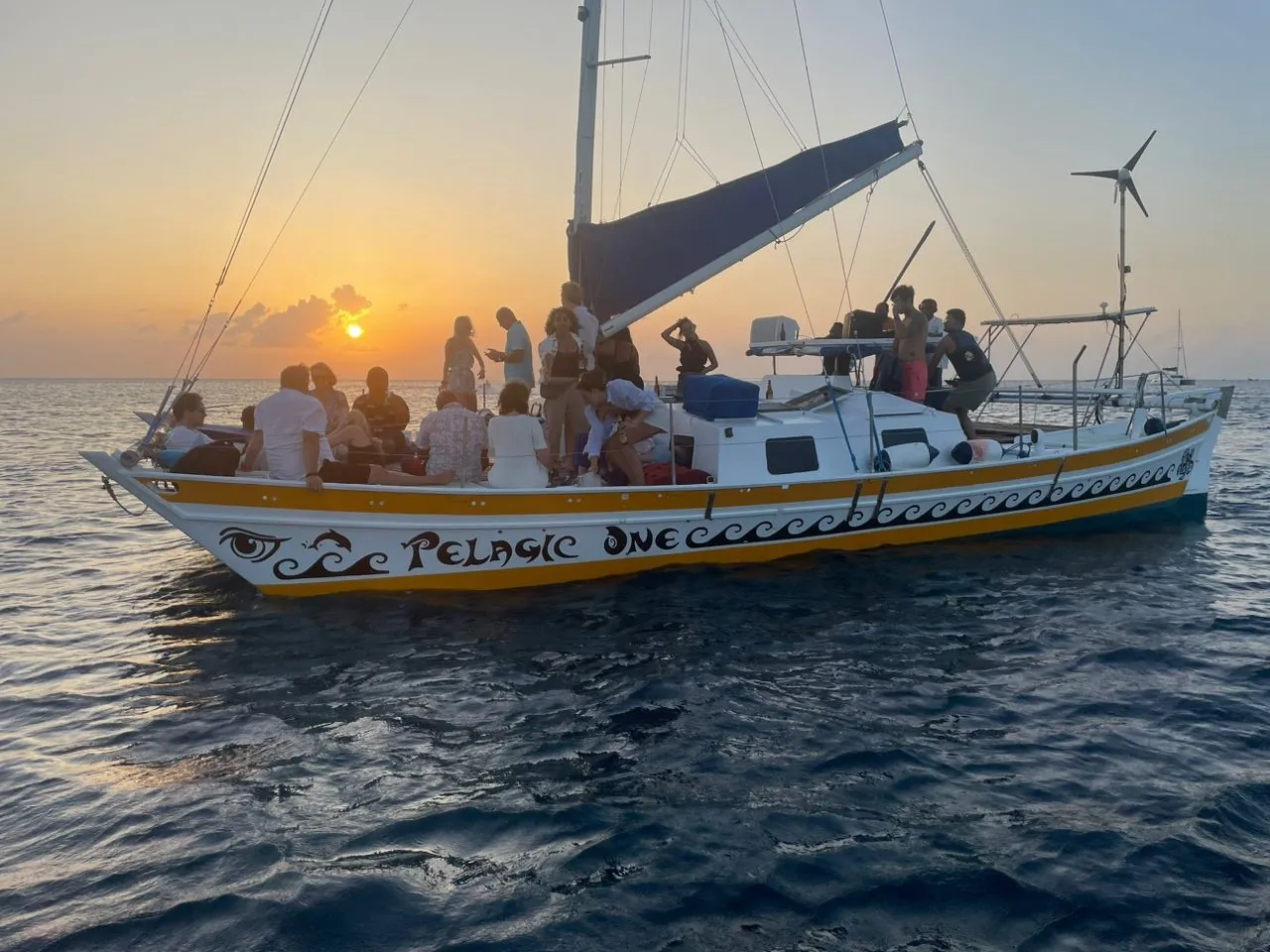 Guests on the deck of a yellow-and-white catamaran at sunset