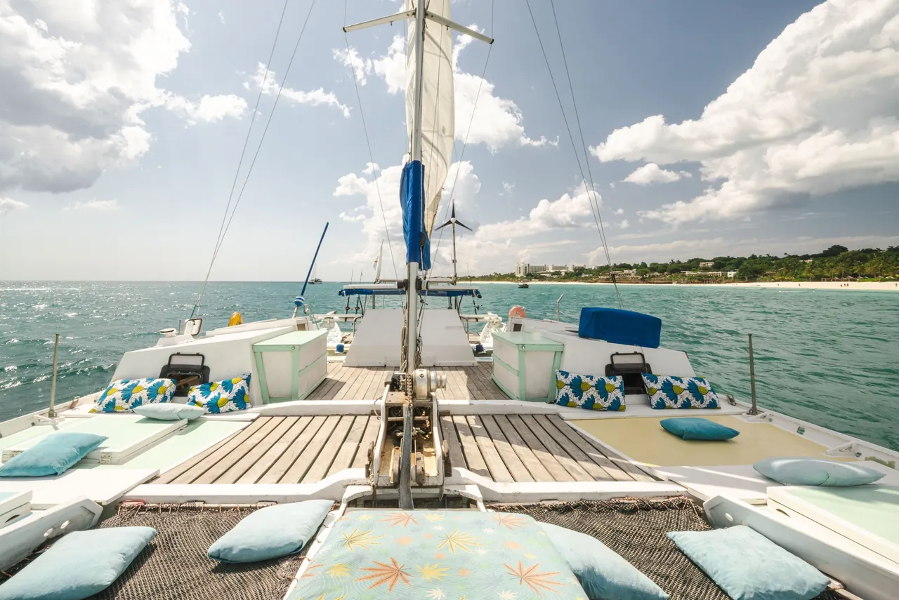Wide view along a catamaran deck towards the mast and the shore