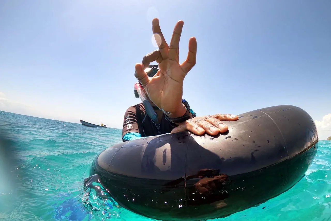 Snorkeller holding an inflatable ring giving an OK sign at the surface
