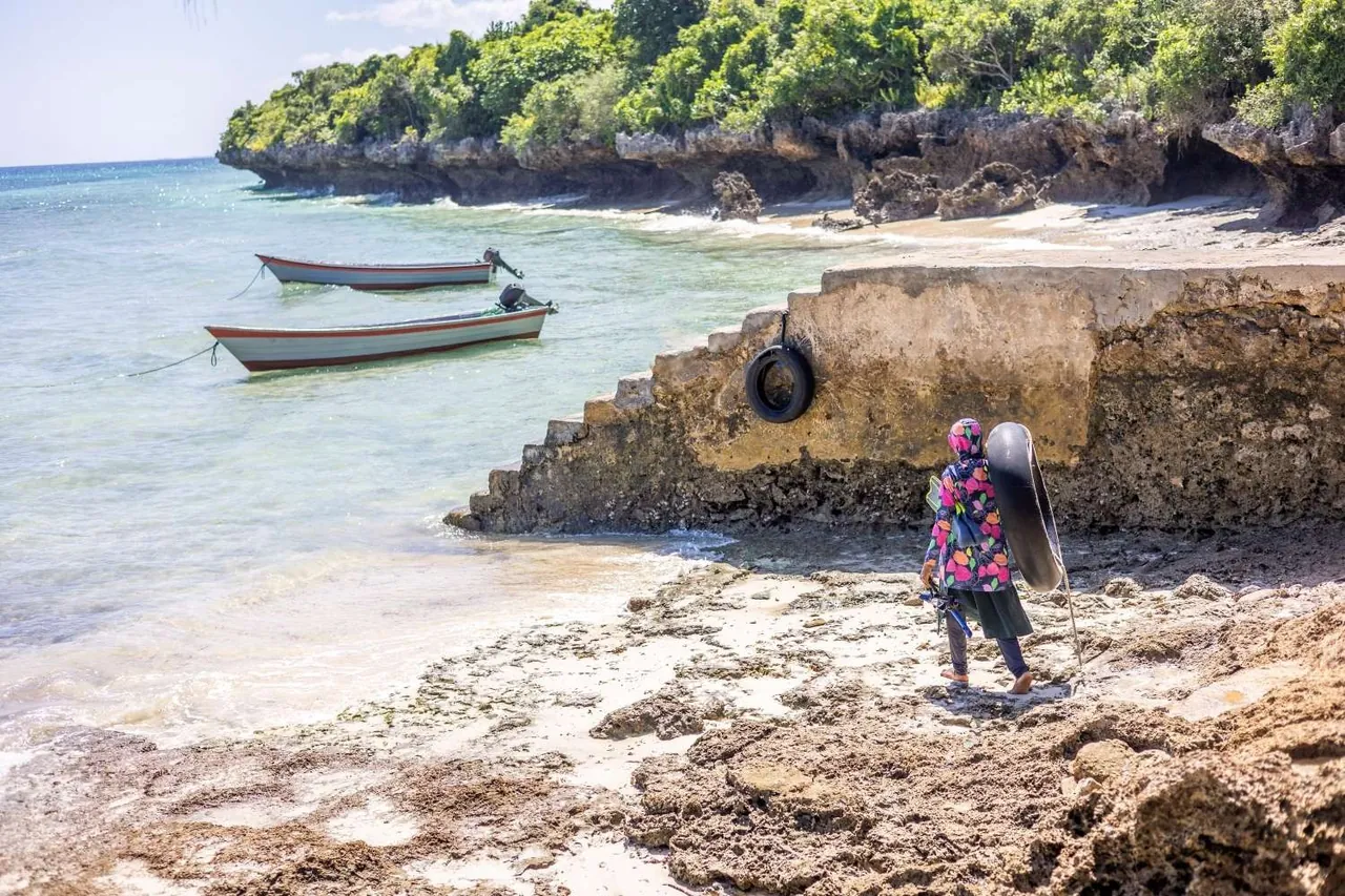 Person carrying an inner-tube float across a rocky shore to the water