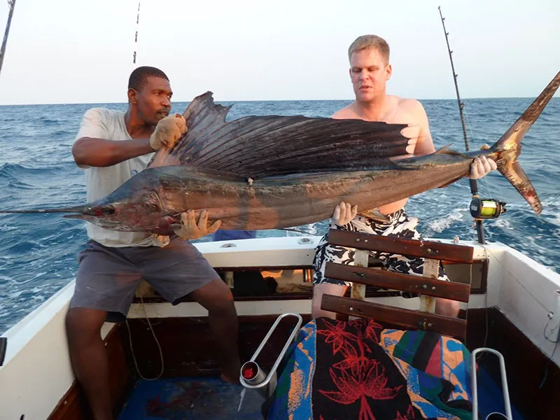 Crew and an angler holding a sailfish across the deck of a sportfishing boat