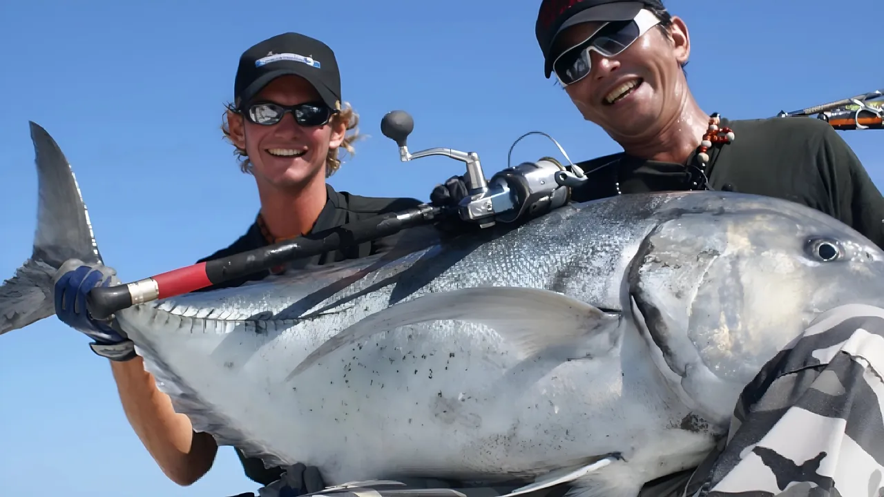 Two smiling anglers holding a large giant trevally