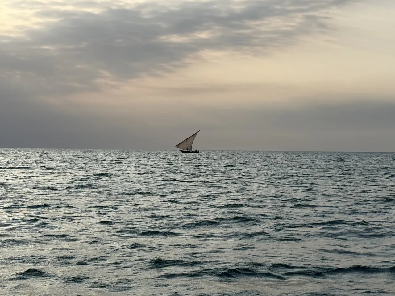 A small dhow under sail on a grey sea under a hazy sky