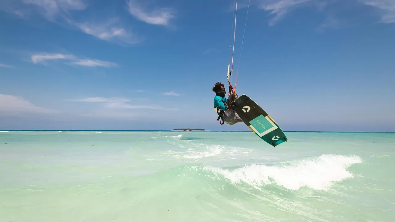 A kitesurfer in mid-air over shallow water with a small island on the horizon