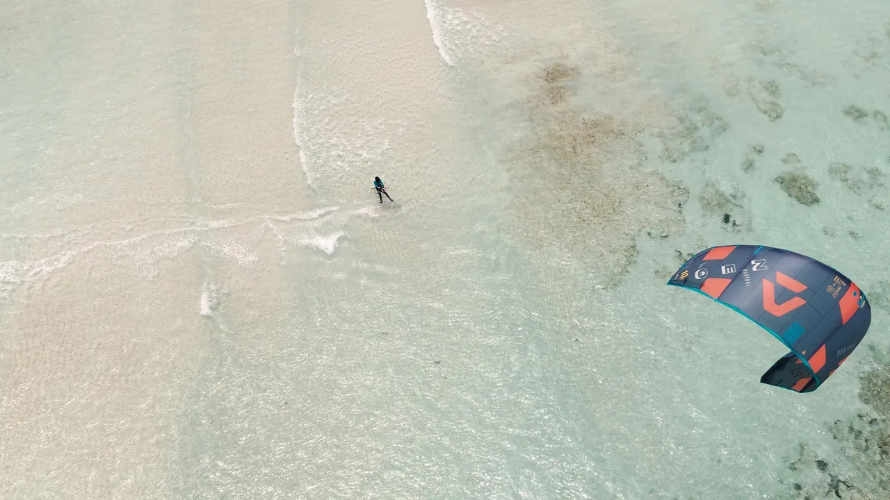 Drone view of a kitesurfer and kite above sand-bottomed shallows and reef patches