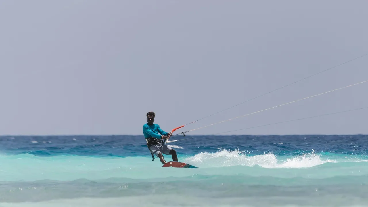 A kitesurfer riding through small waves in deep blue and turquoise water