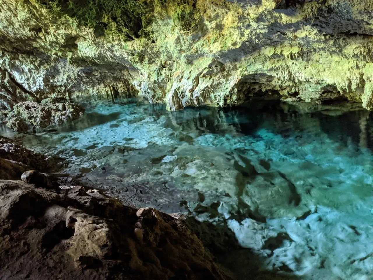 Clear blue-green water filling a low limestone cave