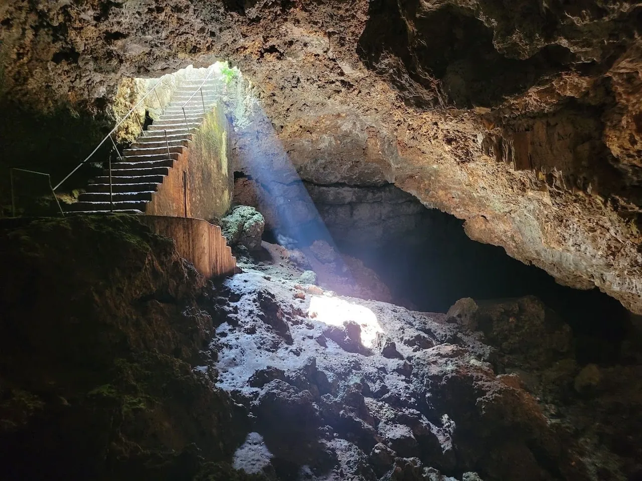 Shaft of light falling through a cave entrance onto rocky floor with steps on the left