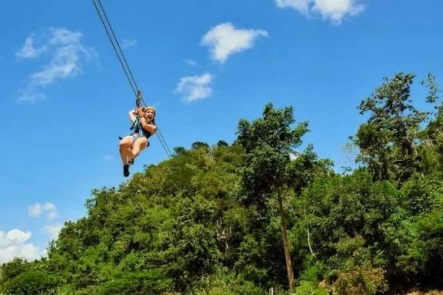Person in a harness gliding on a zipline cable above forest against a blue sky