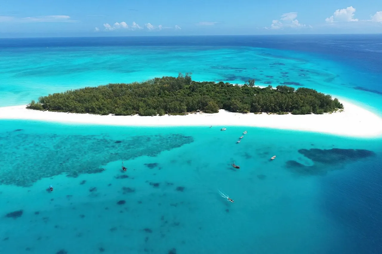 Aerial view of Mnemba Island ringed by white sand, reef and moored boats