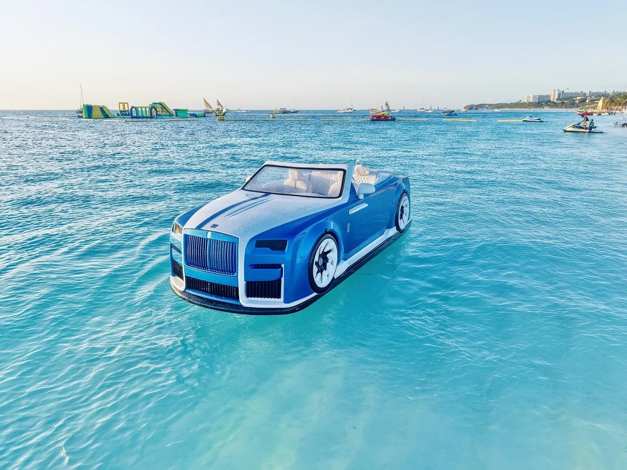 A car-shaped motor boat on turquoise water with an inflatable water park and jet skis behind