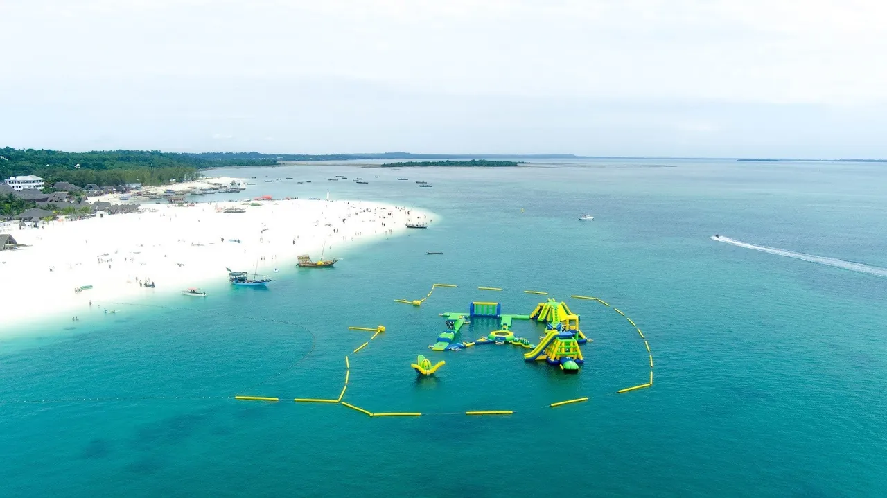 Aerial view of a white beach with an inflatable water park and a buoyed swim zone offshore