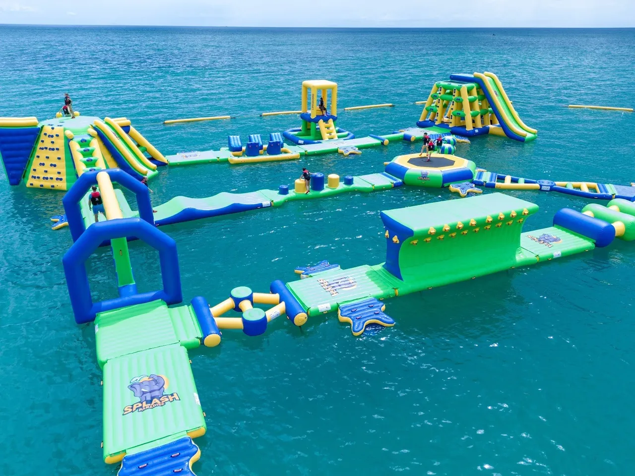 Drone view of a large green, blue and yellow inflatable obstacle course on the sea
