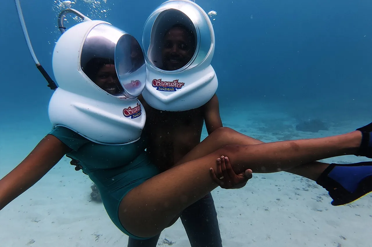 Two people in Seawalker helmets posing on the seabed with the air hose visible