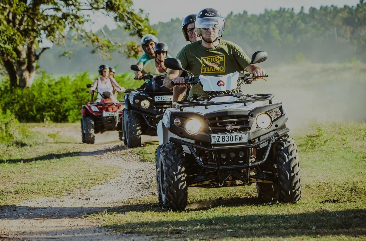 Riders in helmets driving quad bikes in convoy along a grassy dirt track