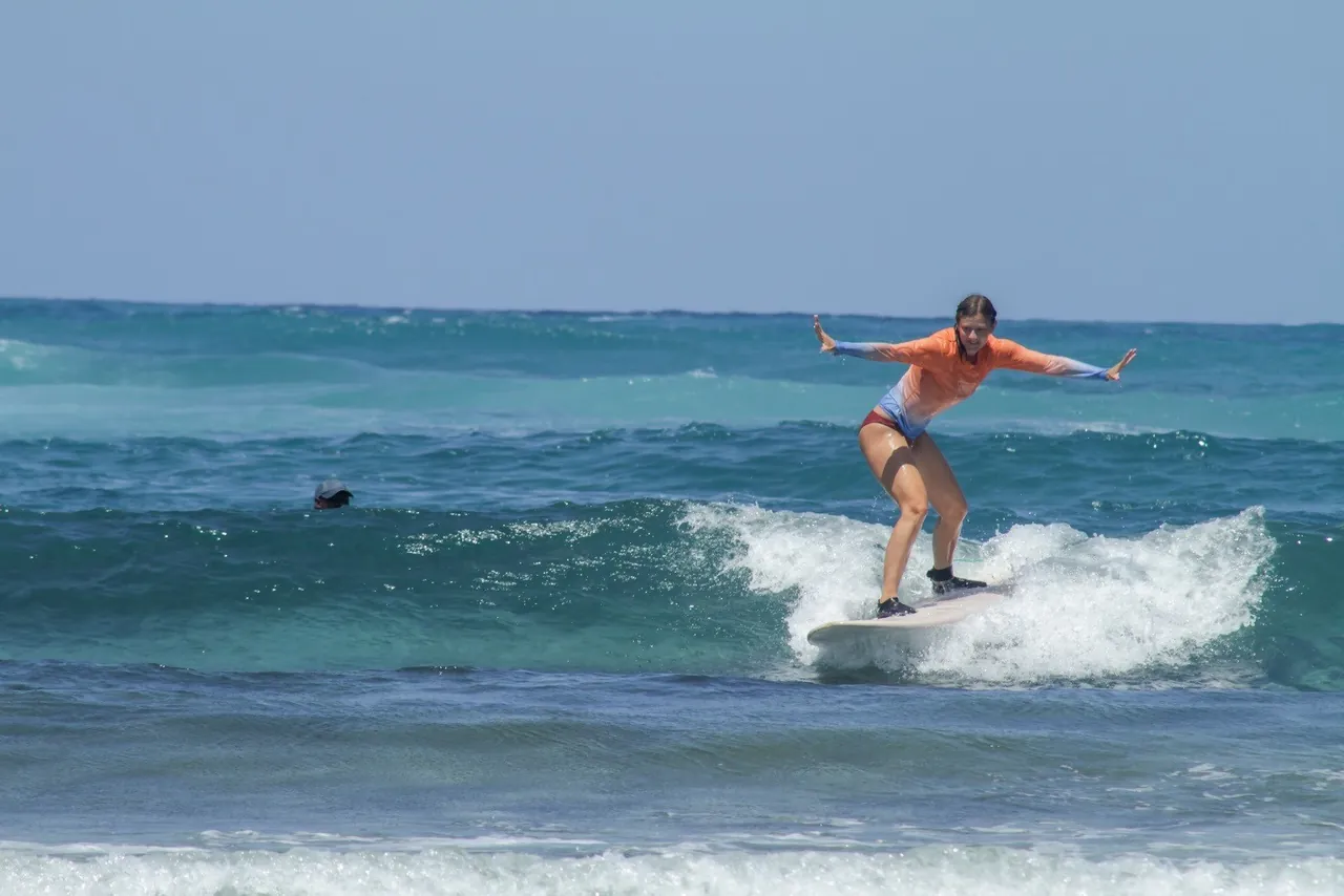 A surfer standing on a board riding white water on a small wave