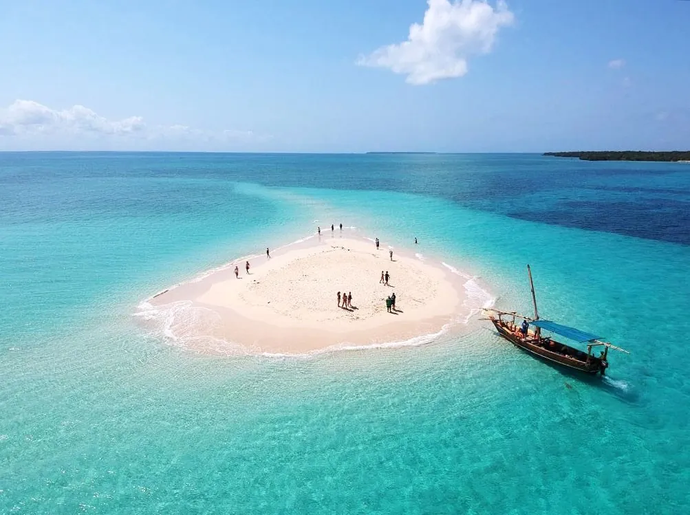 Aerial view of a small sandbank with people and a moored dhow