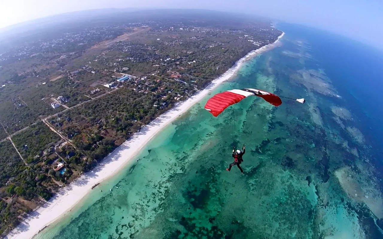 Skydiver under a red canopy above a long white beach and turquoise reef