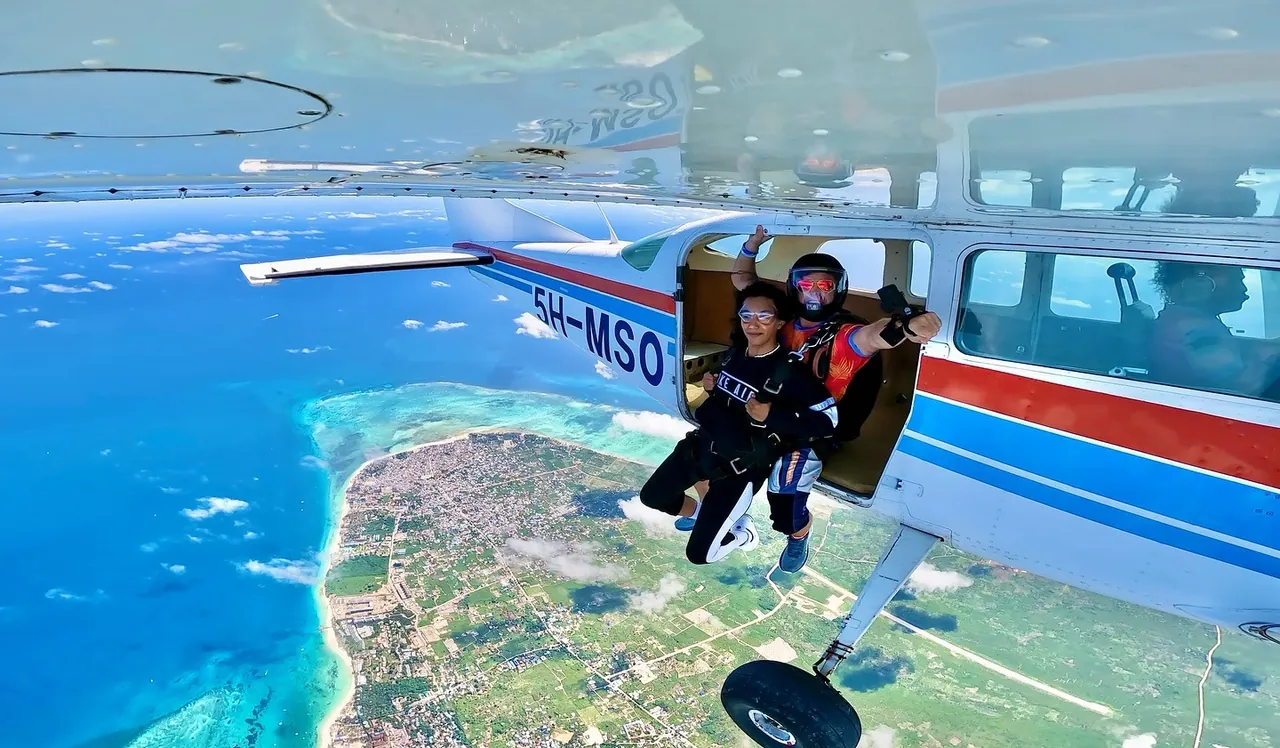 Tandem skydivers leaving a red-white-and-blue Cessna above the Nungwi peninsula