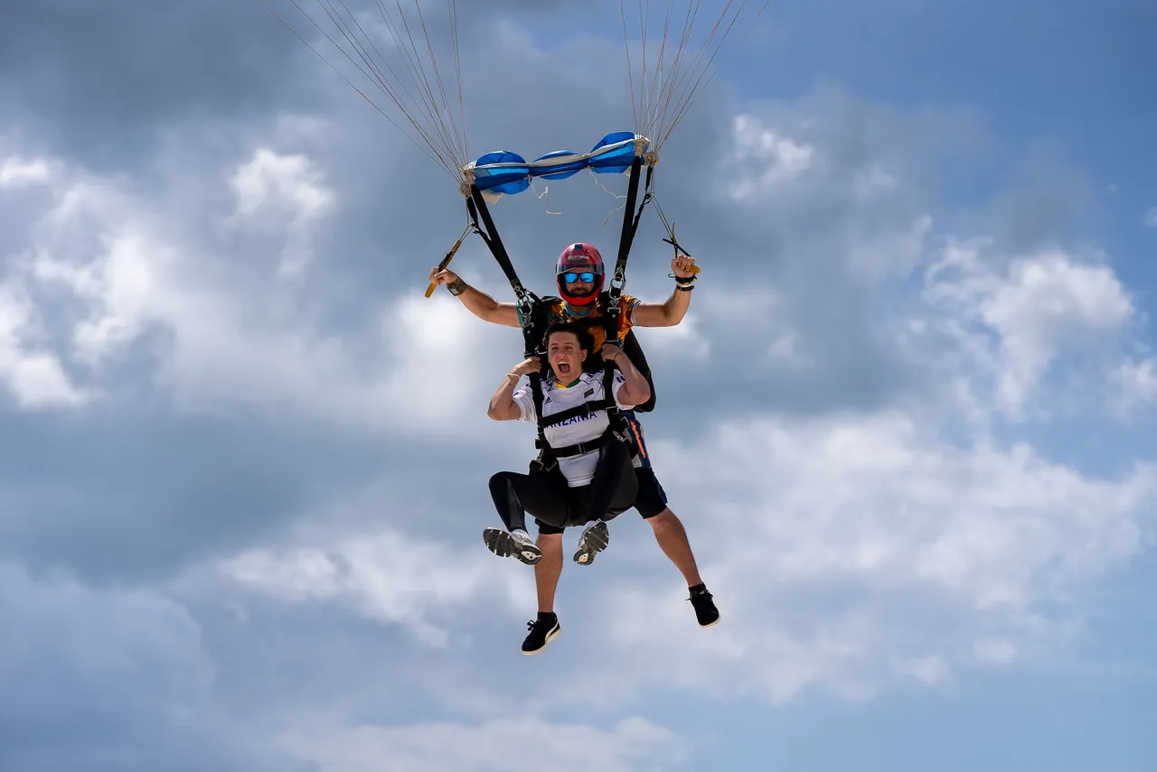 Tandem skydiver and instructor under canopy against a cloudy sky