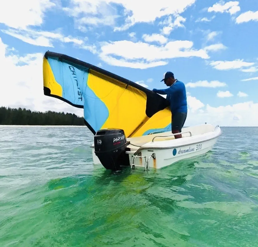 An instructor standing in a small motorboat holding a yellow and blue wing over green shallow water