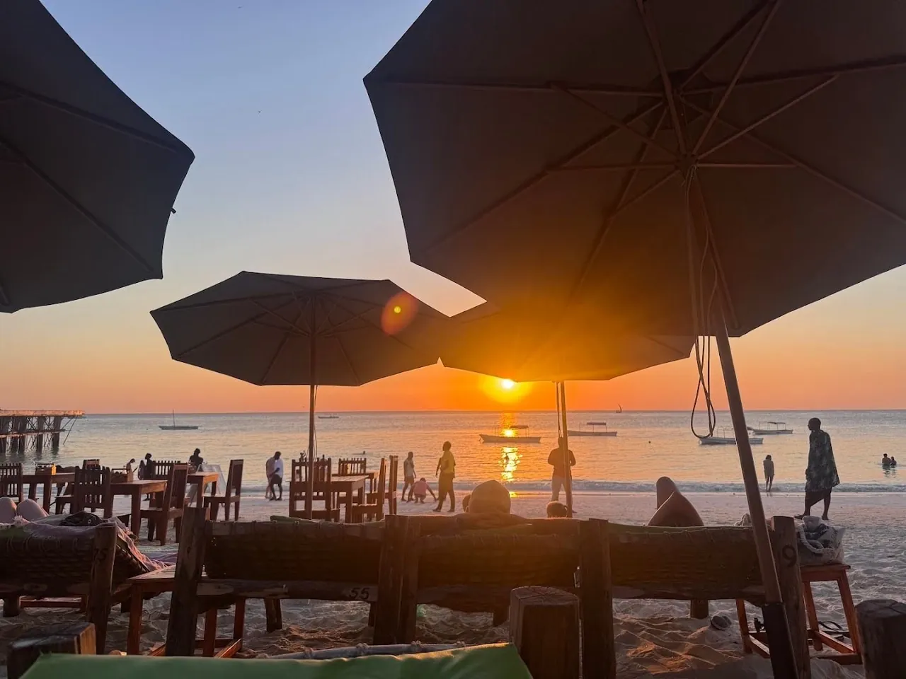 Sun setting between parasols over tables on the beach and the sea