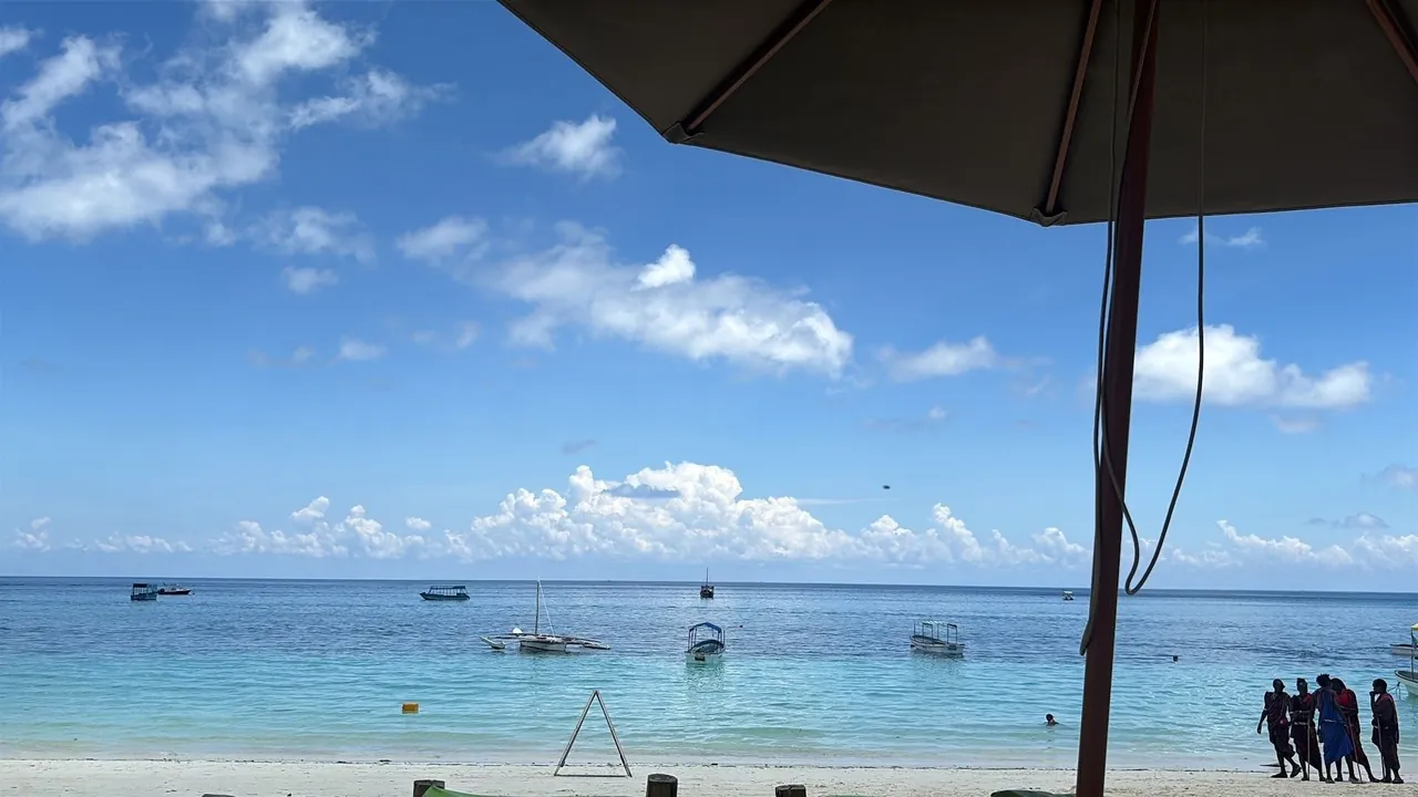 Turquoise sea and boats seen from under a dark beach umbrella
