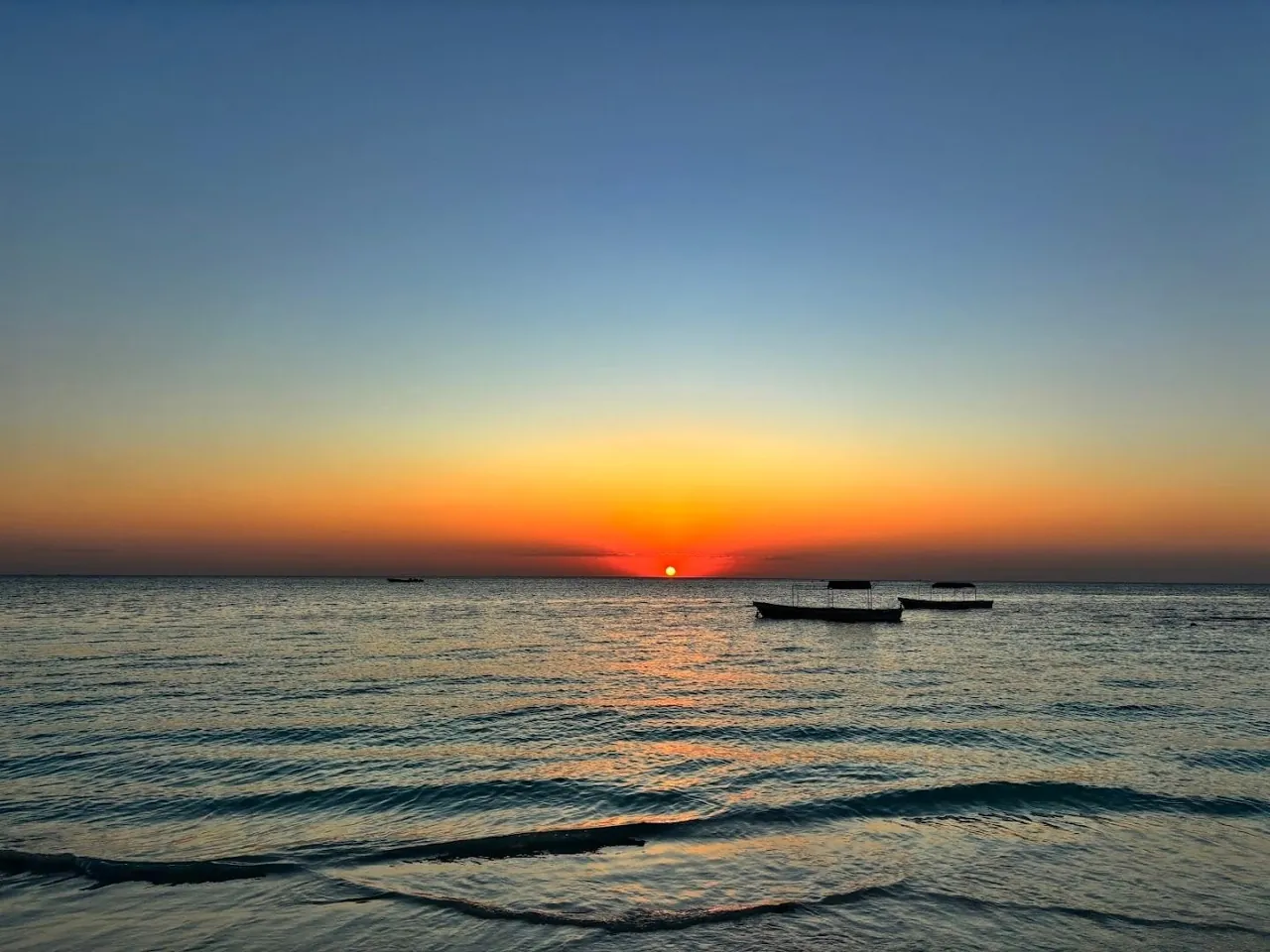 The sun setting over a calm sea with boats on the horizon