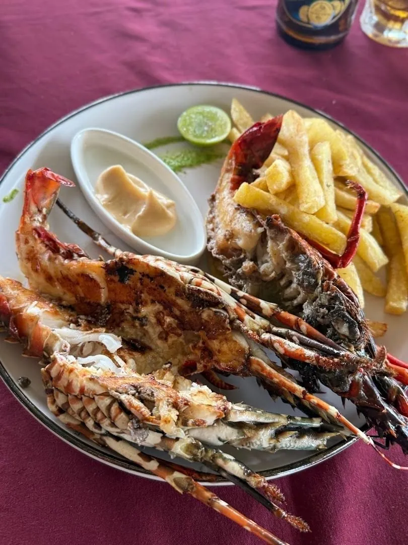 A plate of grilled lobster with chips, lime and a small dish of sauce on a red tablecloth.