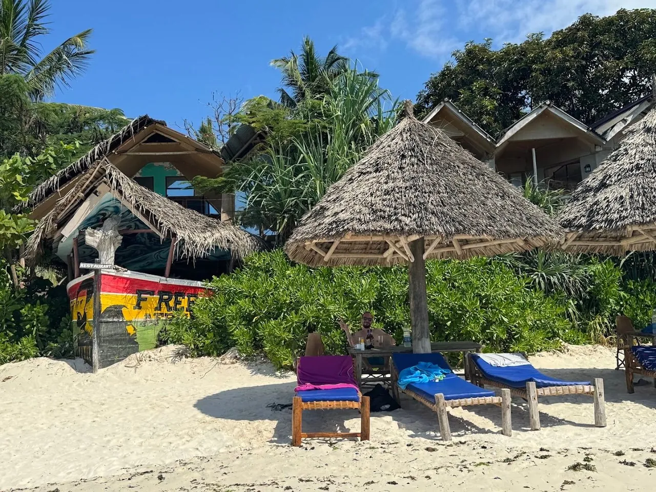 Sun loungers and a thatched parasol in front of the bar and a painted half-dhow