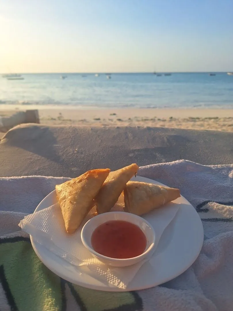 A plate of samosas with chilli sauce on a table by the beach at sunset