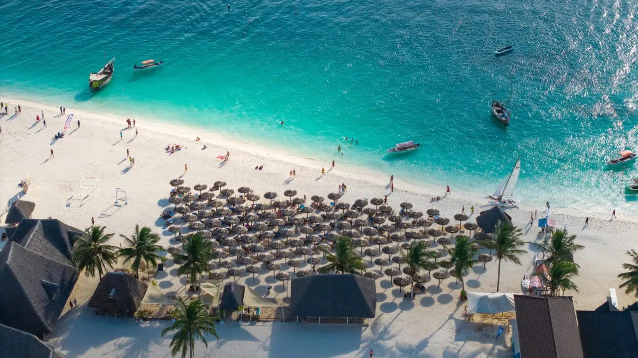 Aerial view of Kendwa beach with rows of thatched parasols, turquoise water and boats