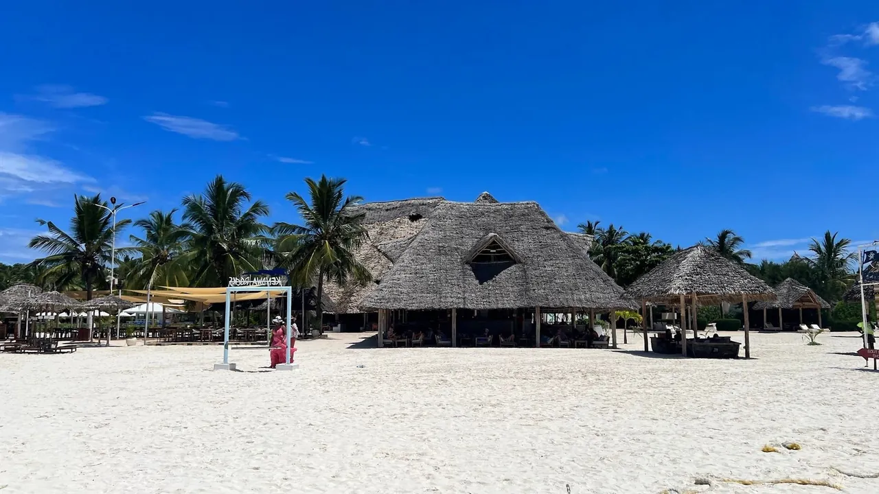 Large thatched beach restaurant on white sand under a deep blue sky