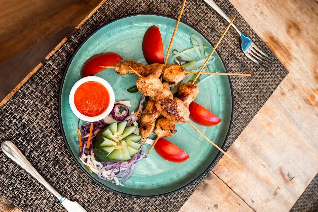 Chicken skewers with tomatoes and chilli sauce on a turquoise plate