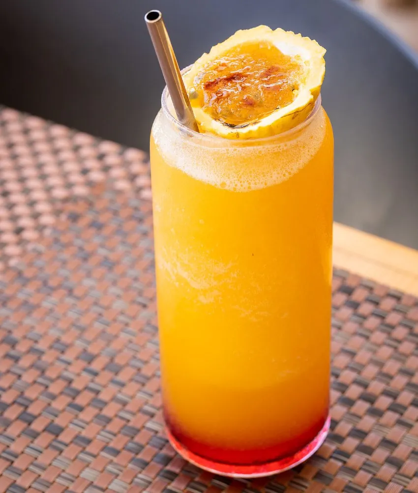 An orange and red layered cocktail in a tall glass with a straw