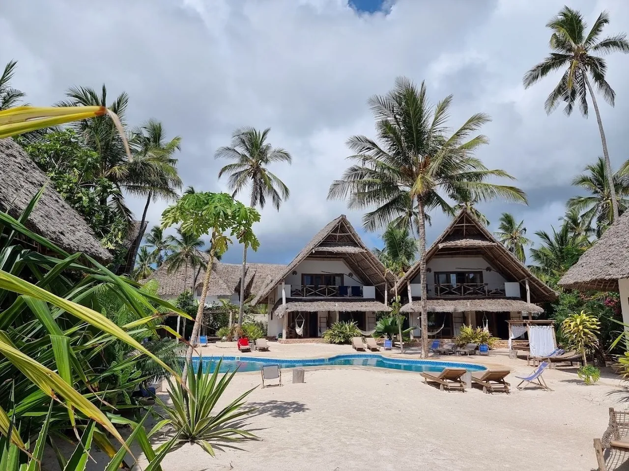 Thatched two-storey bungalows around a swimming pool among palm trees.