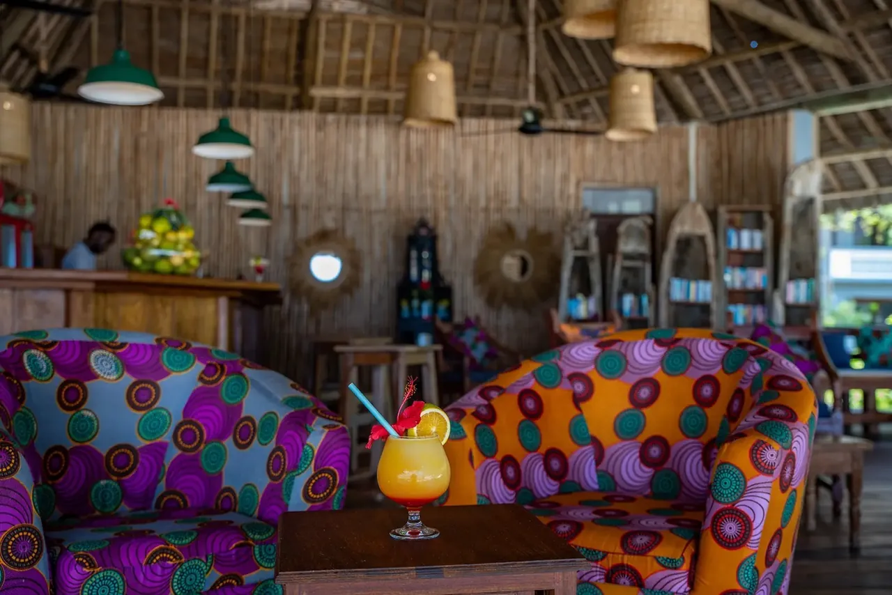 A bar lounge with colourful African-print armchairs, wicker lamps and a cocktail on a low table.