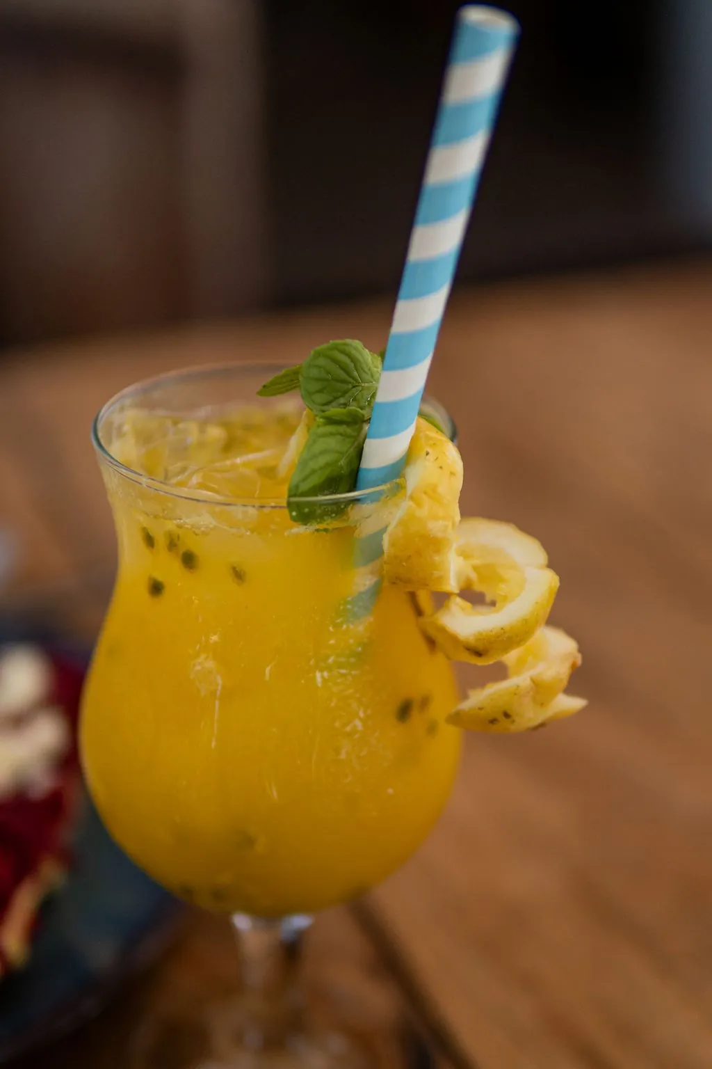 A tall orange cocktail with a striped straw and lime on a wooden table.