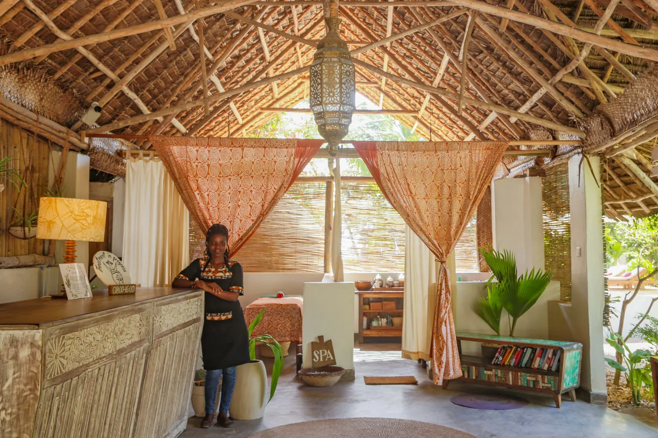 A café interior under a high thatched roof, with curtains, a counter and plants.