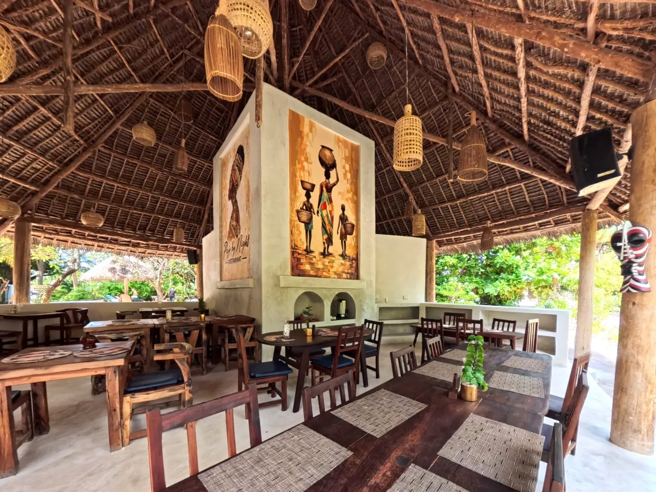 An open-sided thatched restaurant with wooden tables and a painted pillar in the middle.