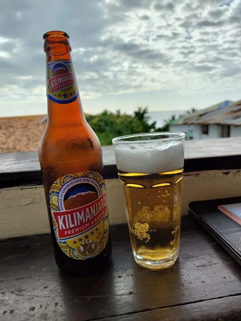 A bottle of Kilimanjaro beer and a glass on a wooden ledge with sky and trees behind