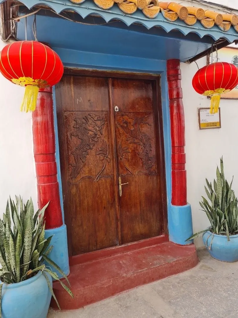 A carved wooden double door framed in red and blue with red paper lanterns and potted plants