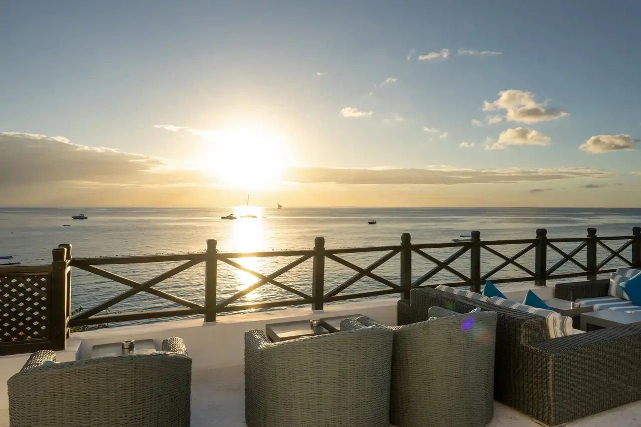 Low armchairs on a rooftop terrace facing the sun setting over the sea