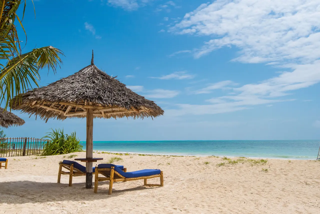 A thatched umbrella and two loungers on white sand facing the turquoise sea