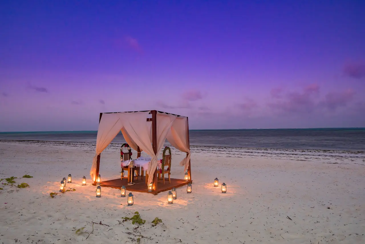 A canopied dinner table on the beach lit by lanterns at twilight
