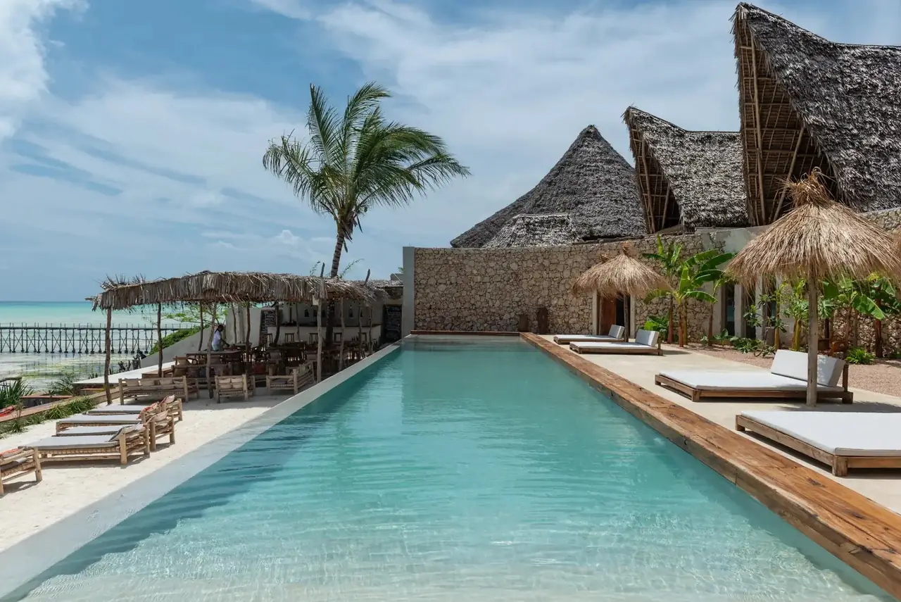 A long pool with loungers in front of steep thatched roofs