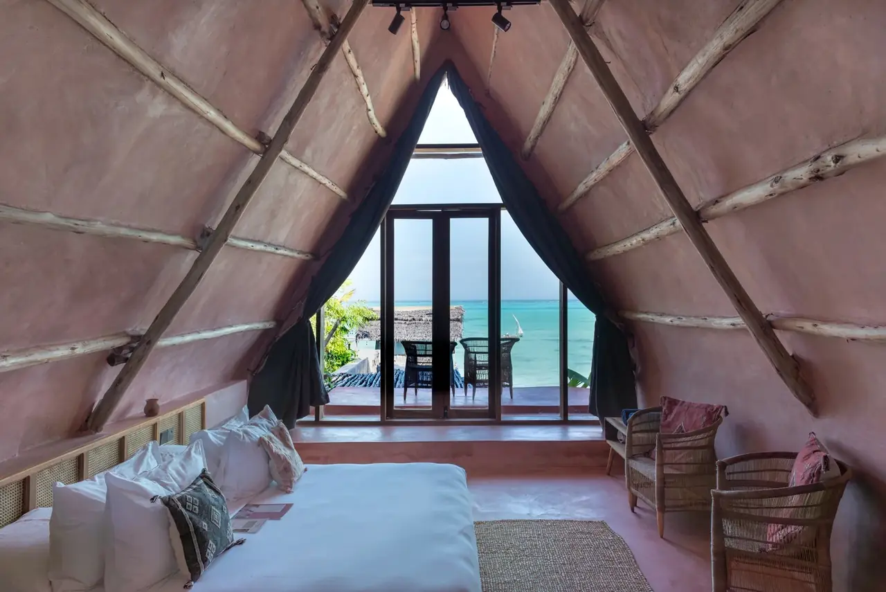 A bedroom under an A-shaped roof with a window to the sea