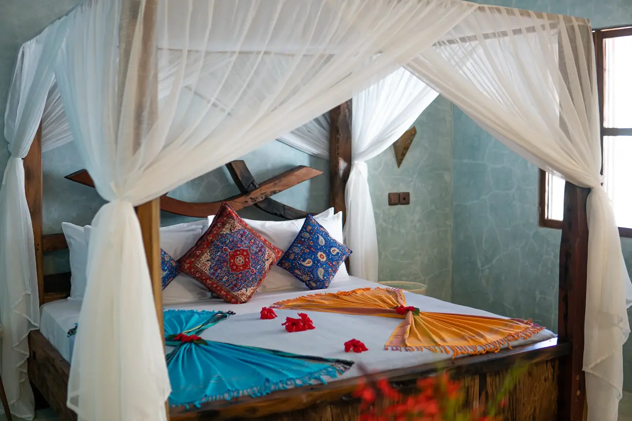 A four-poster bed with colourful cushions and flower petals