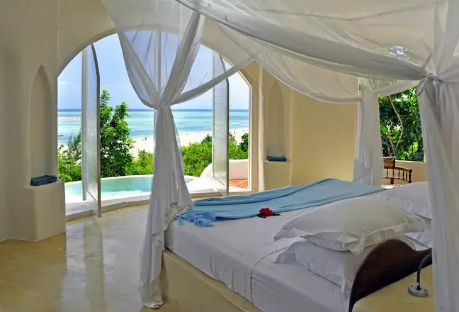 A pavilion bedroom with a draped bed and arched openings to the plunge pool and sea