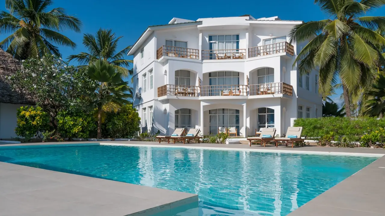 A white three-storey building with balconies behind a pool